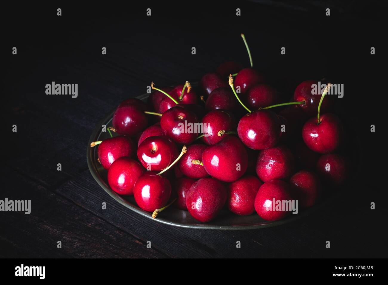 Cerises rouges foncé sur une assiette de étain. Faible luminosité, gros plan horizontal. Banque D'Images