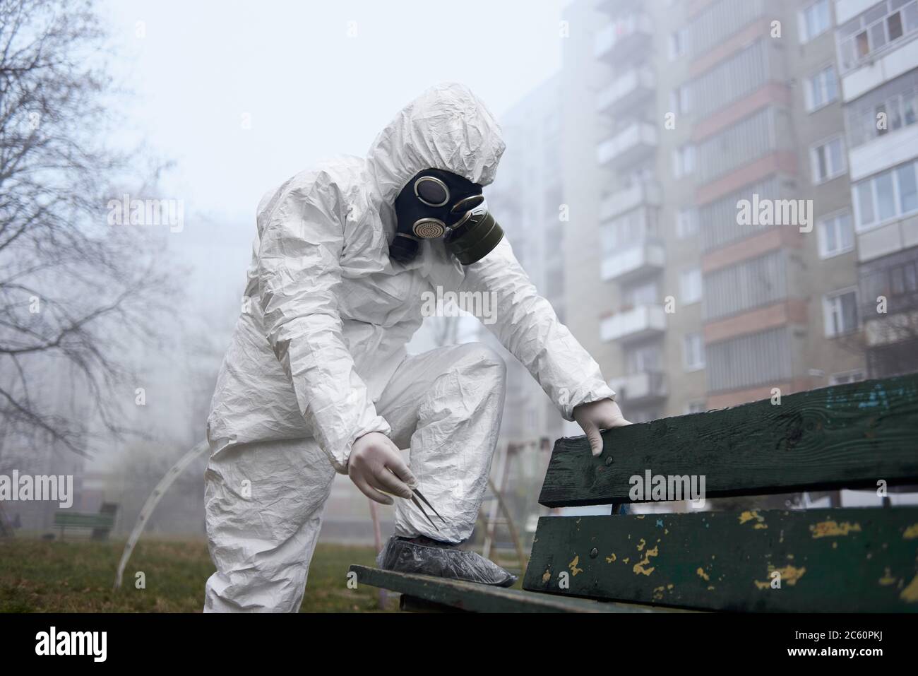Chercheur scientifique tenant des pinces tout en étant debout sur banc. Homme écologiste portant un uniforme de protection, des gants, des couvre-chaussures et un masque à gaz tout en explorant les problèmes environnementaux dans la rue Banque D'Images