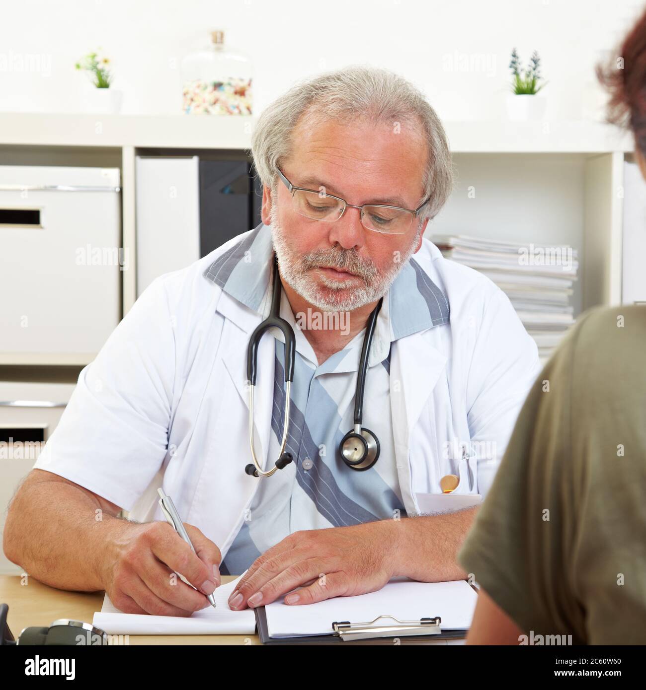 Le médecin âgé, en consultation, prend des notes avec un patient Banque D'Images