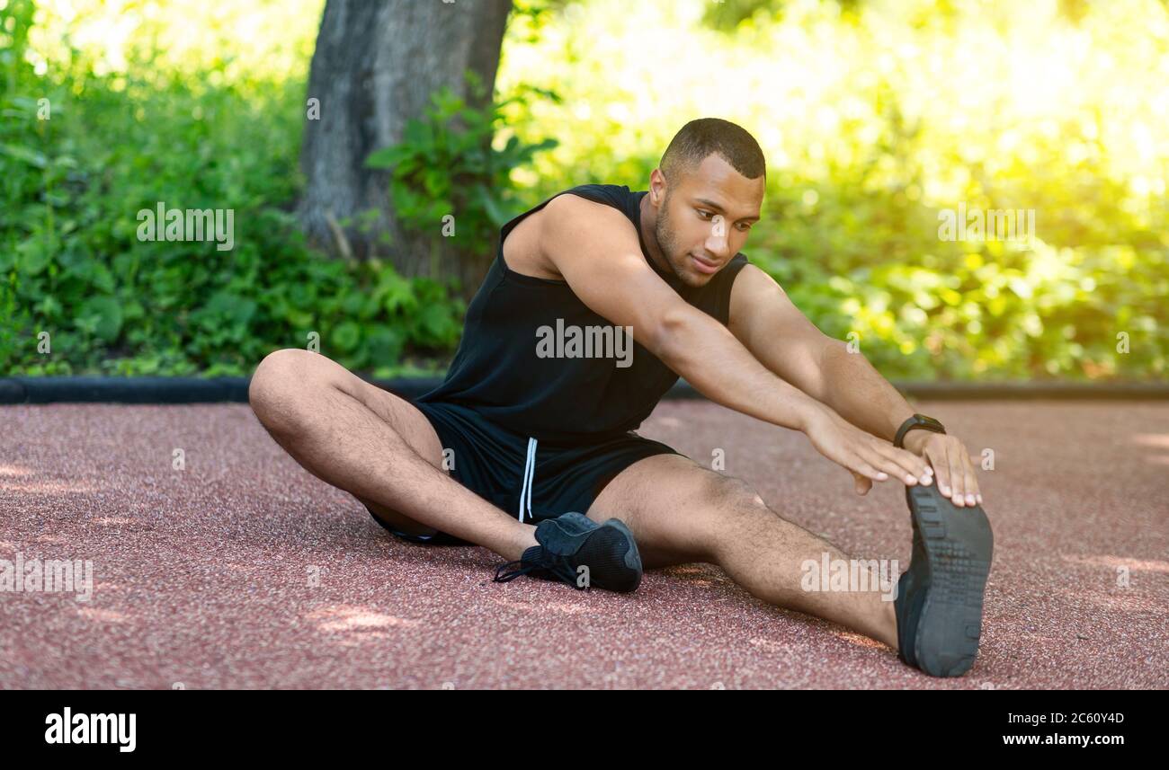 Sportif afro-américain qui s'étend les jambes sur une piste de jogging au parc Banque D'Images