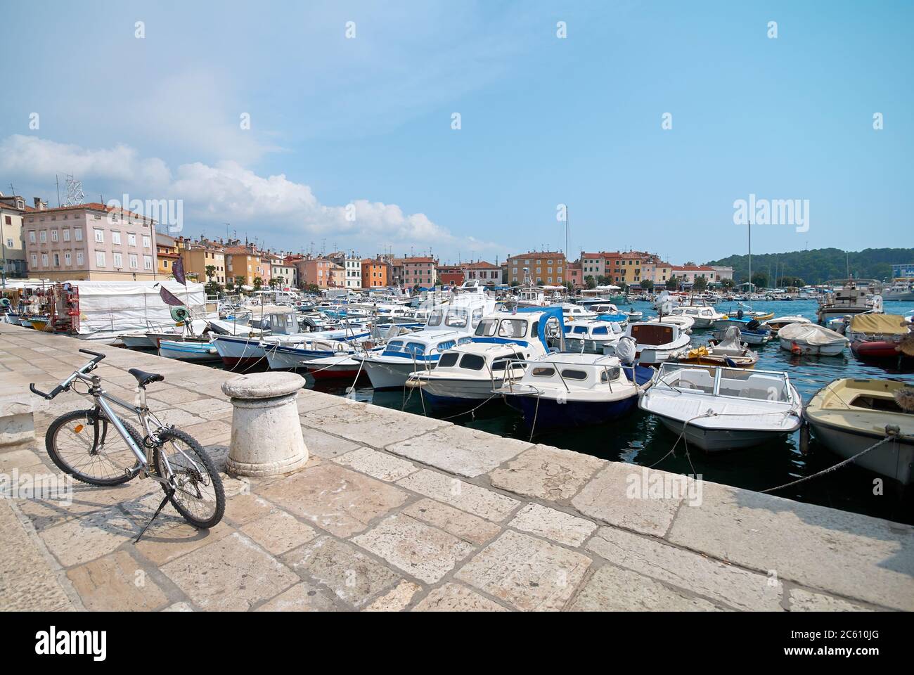 Le vélo est stationné sur la jetée du port de Rovinj, en Croatie. Yachts débarquant, bateaux à moteur et bateaux sur l'eau, maisons médiévales anciennes de la vieille ville sur le b Banque D'Images