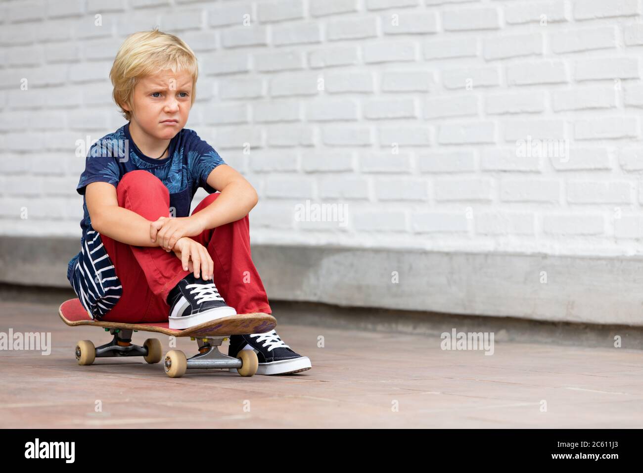 Le patineur qui a l'air malheureux et contrarié s'assoit sur le skateboard avant que les enfants s'entraîne dans le parc de skate vie familiale active, activités de loisirs en plein air Banque D'Images