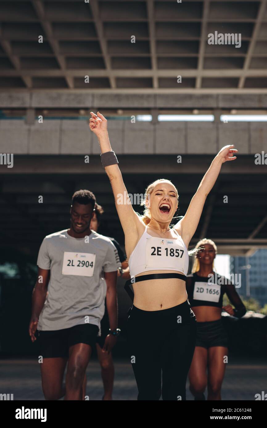 Sportswoman franchit la ligne d'arrivée en premier et remporte la course de marathon. Femme qui court dans la foule et traverse la ligne d'arrivée. Banque D'Images