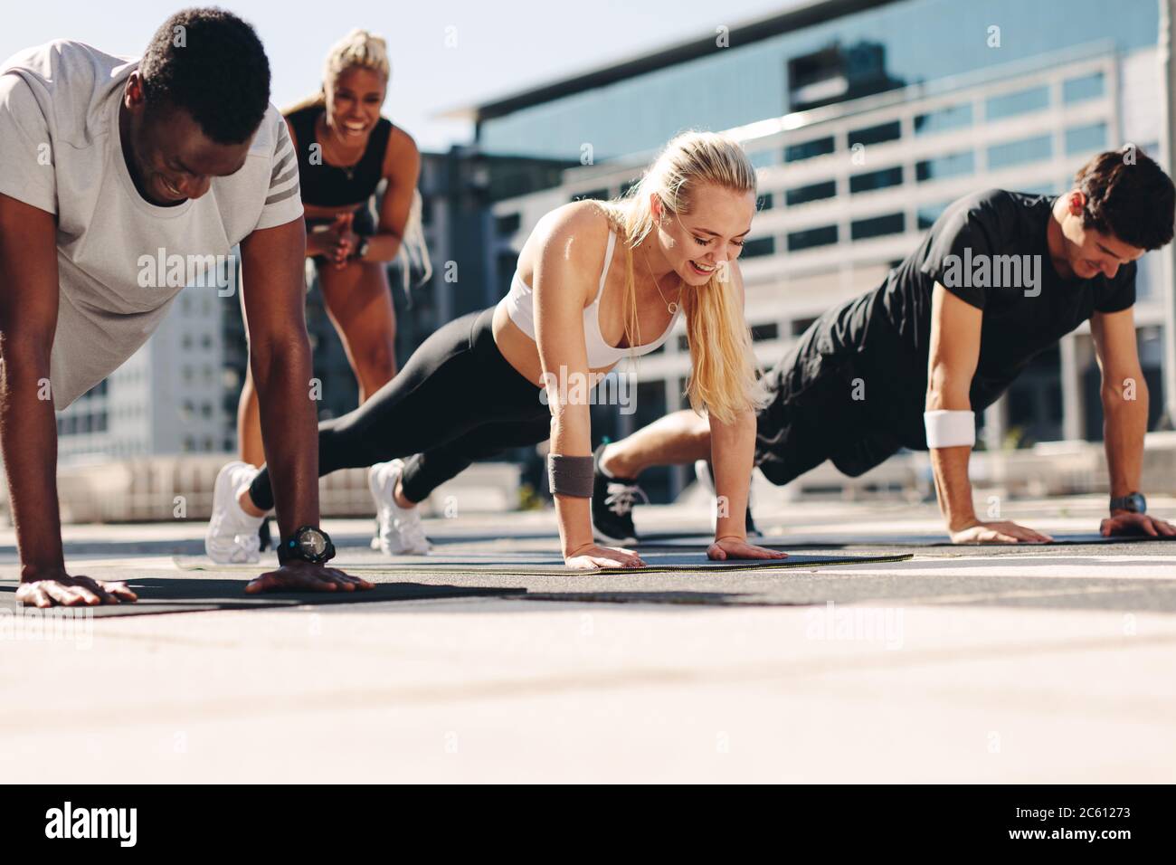 hommes et femmes de fitness faisant des pompes avec la motivation de leur entraîneur féminin en plein air dans la ville. Banque D'Images