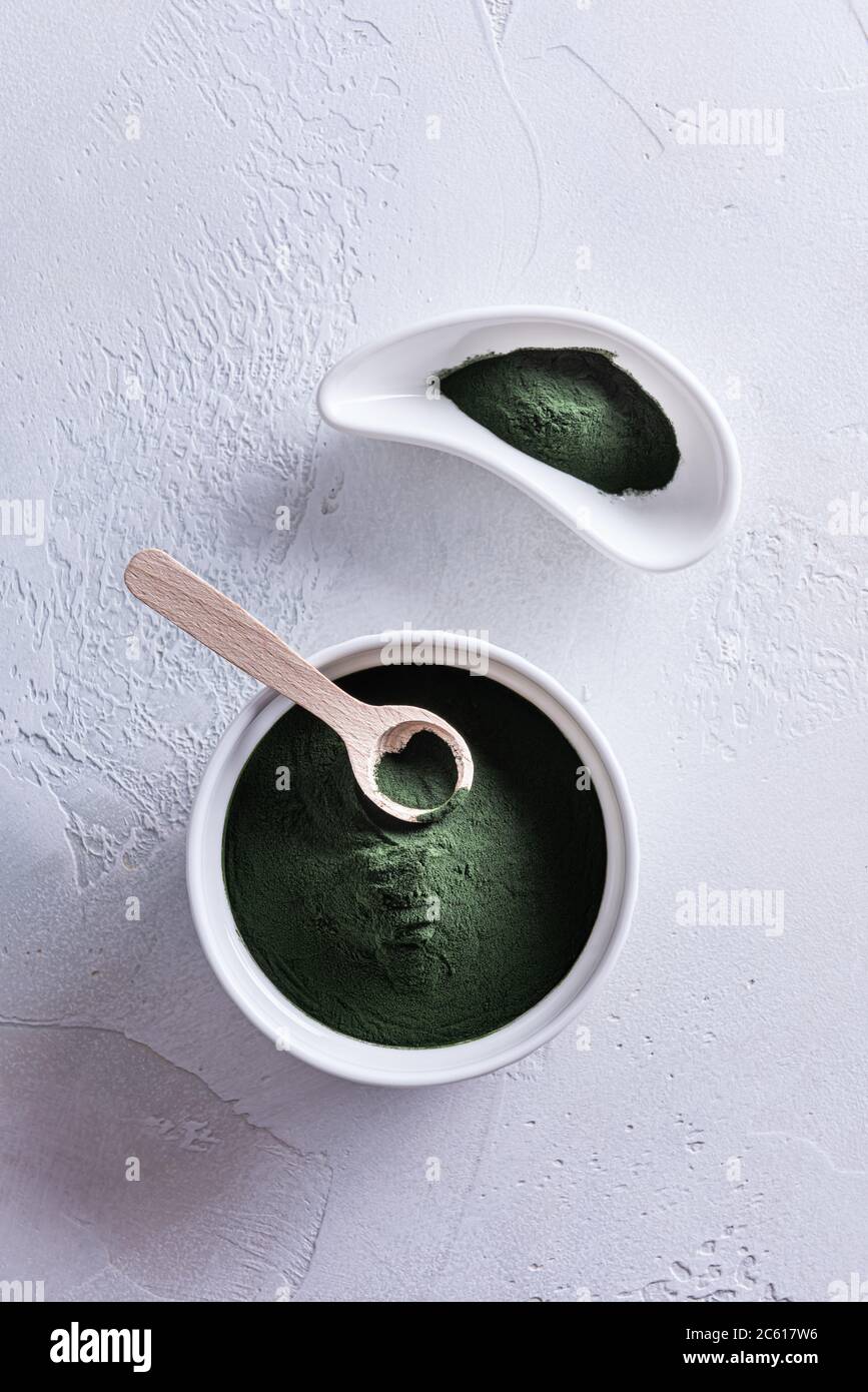 Poudre de chlorelle ou de spiruline verte dans deux bols en porcelaine blanche de forme différente et dans une petite cuillère en bois sur fond blanc. Aliments sains et suralimentaires Banque D'Images