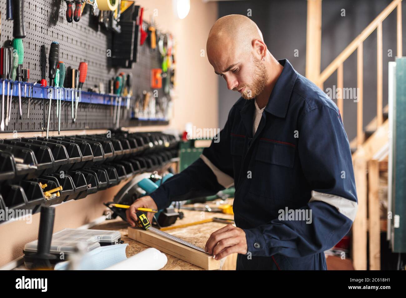 Jeune contremaître dans les vêtements de travail utilisant le ruban de mesure passant du temps Banque D'Images