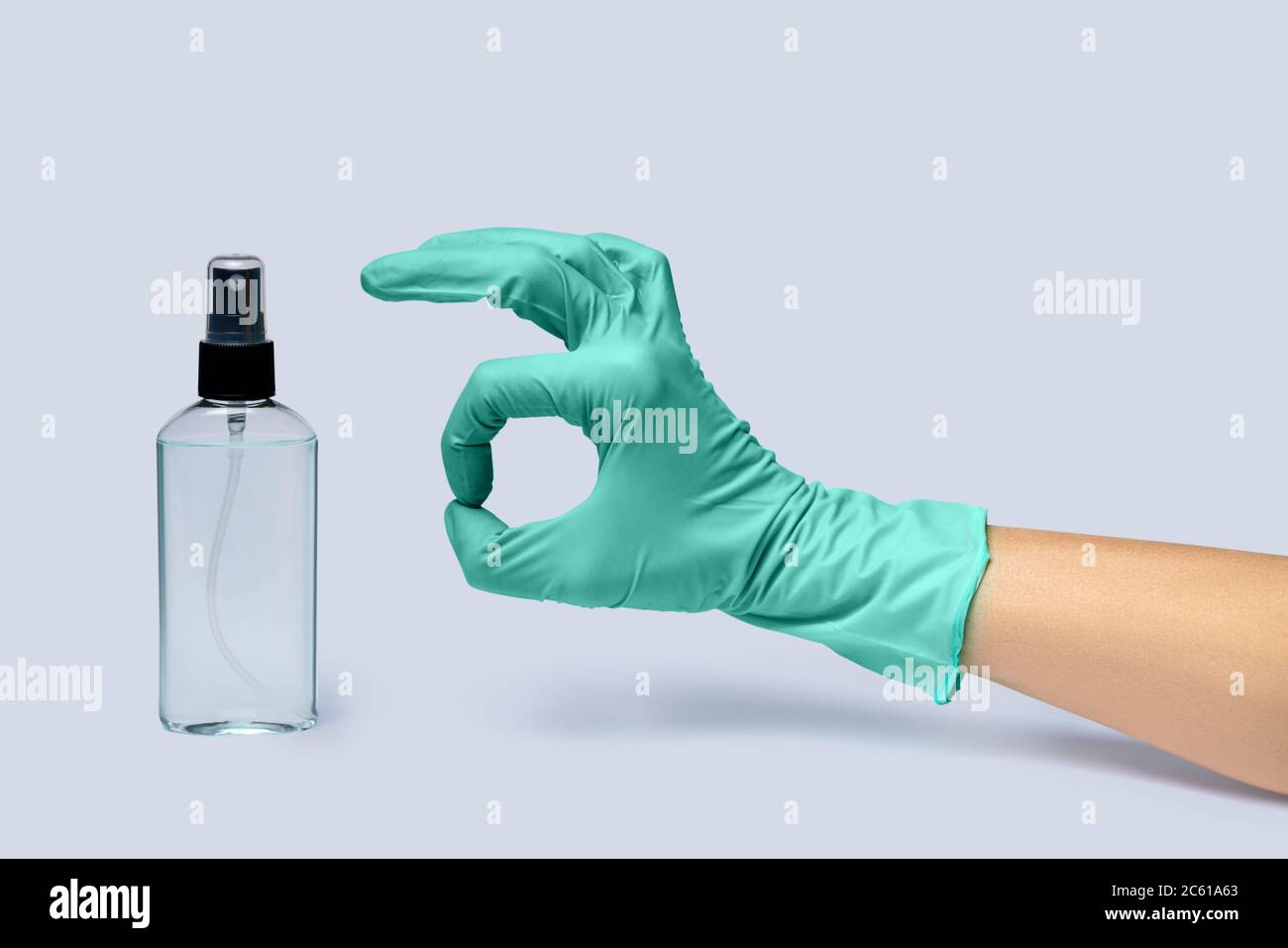 Une femme se tient dans un gant en latex et un distributeur de désinfectant pour les mains sur fond gris clair Banque D'Images