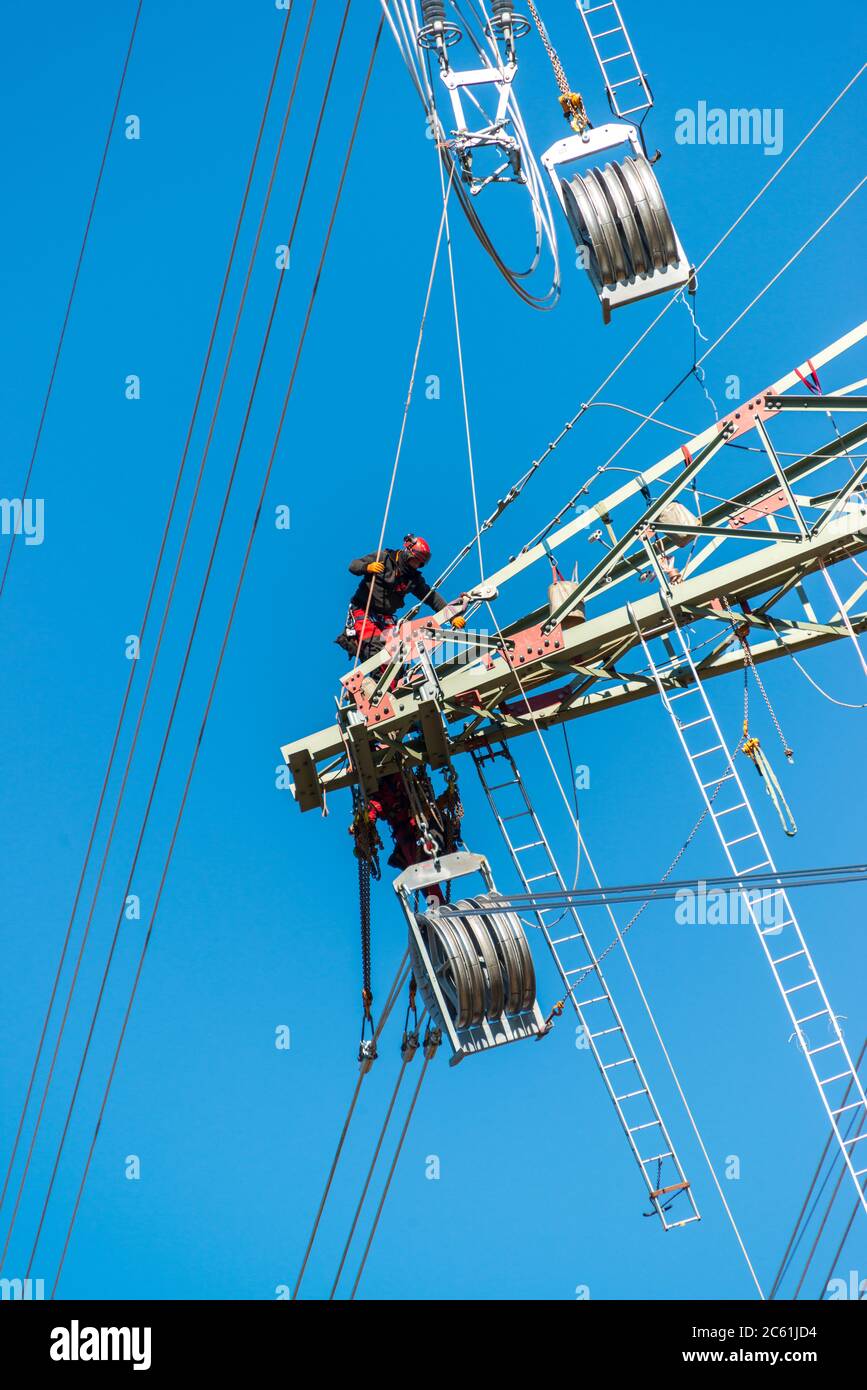Arbeiter auf einem Hochspannungsmast vor blauem wolkenlosen Himmel Banque D'Images