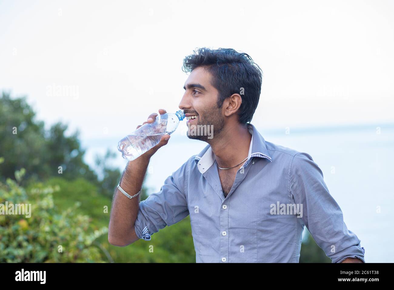 Hydratez-vous. Homme souriant en profil sur le point de boire d'une bouteille d'eau isolé nature arbres et fond de mer Banque D'Images