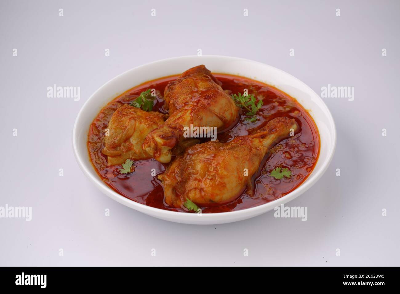 Curry de poulet ou masala, plat épicé de morceaux de poulet rouge garni de feuilles de coriandre et disposé dans un bol blanc avec fond blanc Banque D'Images