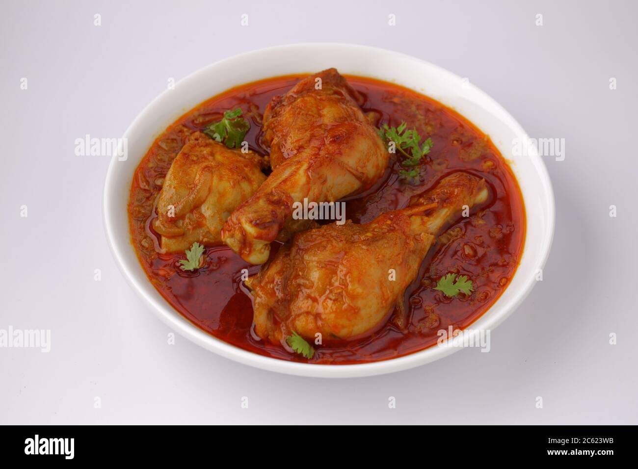 Curry de poulet ou masala, plat épicé de morceaux de poulet rouge garni de feuilles de coriandre et disposé dans un bol blanc avec fond blanc Banque D'Images