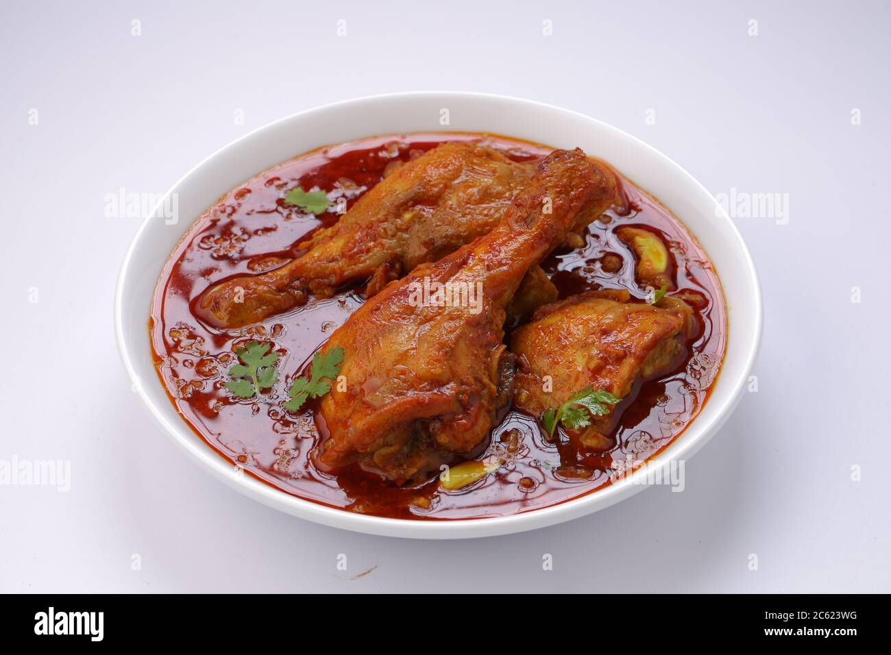 Curry de poulet ou masala, plat épicé de morceaux de poulet rouge garni de feuilles de coriandre et disposé dans un bol blanc avec fond blanc Banque D'Images