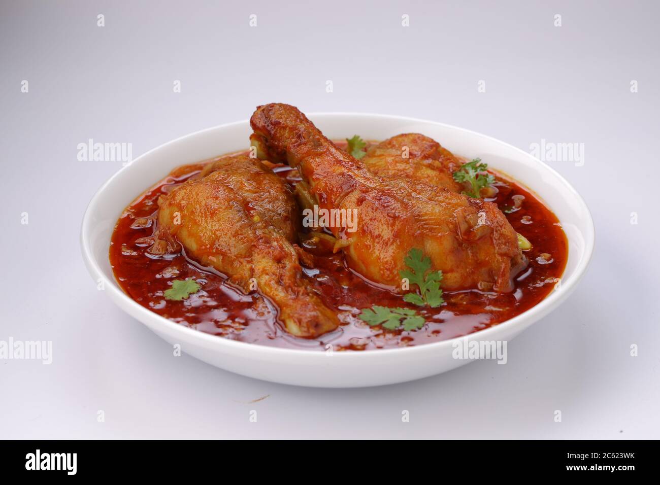 Curry de poulet ou masala, plat épicé de morceaux de poulet rouge garni de feuilles de coriandre et disposé dans un bol blanc avec fond blanc Banque D'Images