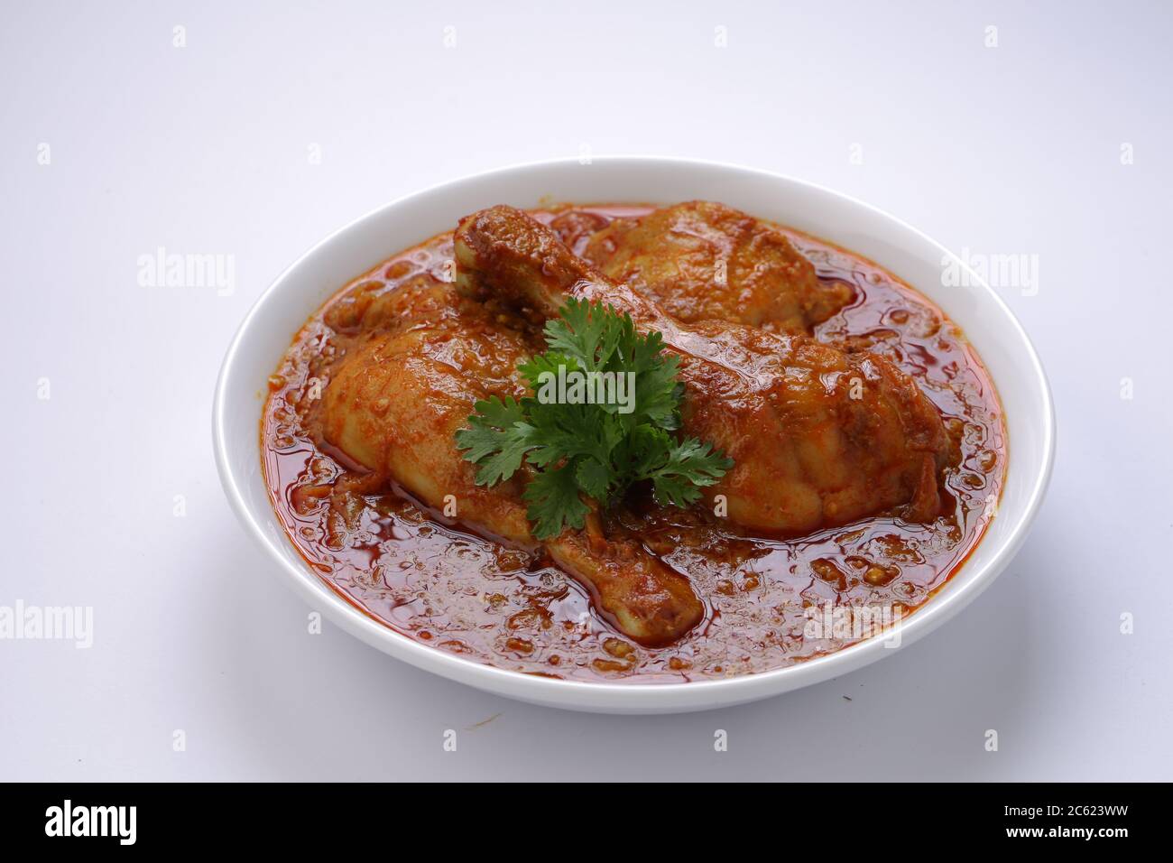 Curry de poulet ou masala, plat épicé de morceaux de poulet rouge garni de feuilles de coriandre et disposé dans un bol blanc avec fond blanc Banque D'Images