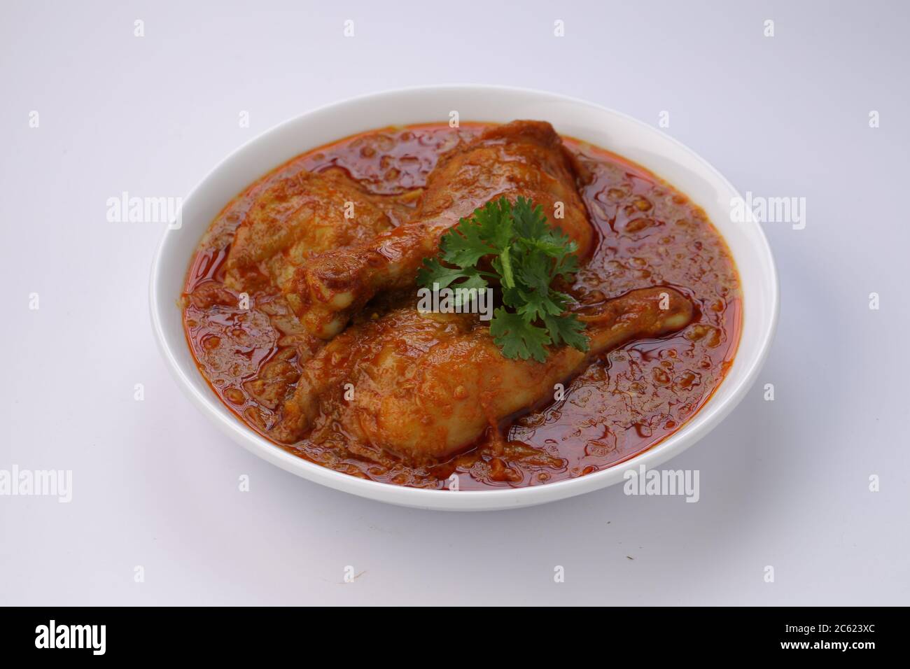 Curry de poulet ou masala, plat épicé de morceaux de poulet rouge garni de feuilles de coriandre et disposé dans un bol blanc avec fond blanc Banque D'Images