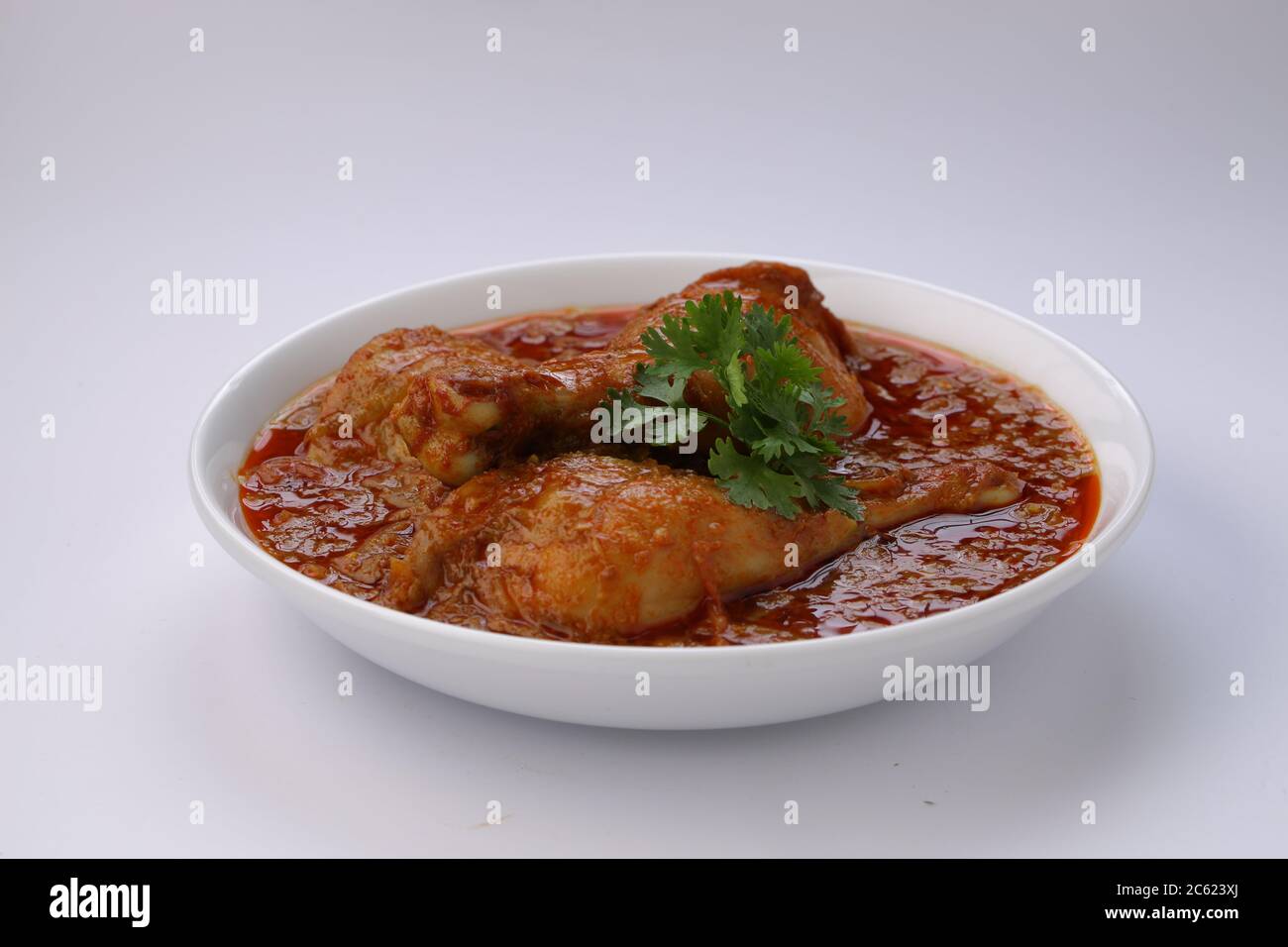 Curry de poulet ou masala, plat épicé de morceaux de poulet rouge garni de feuilles de coriandre et disposé dans un bol blanc avec fond blanc Banque D'Images