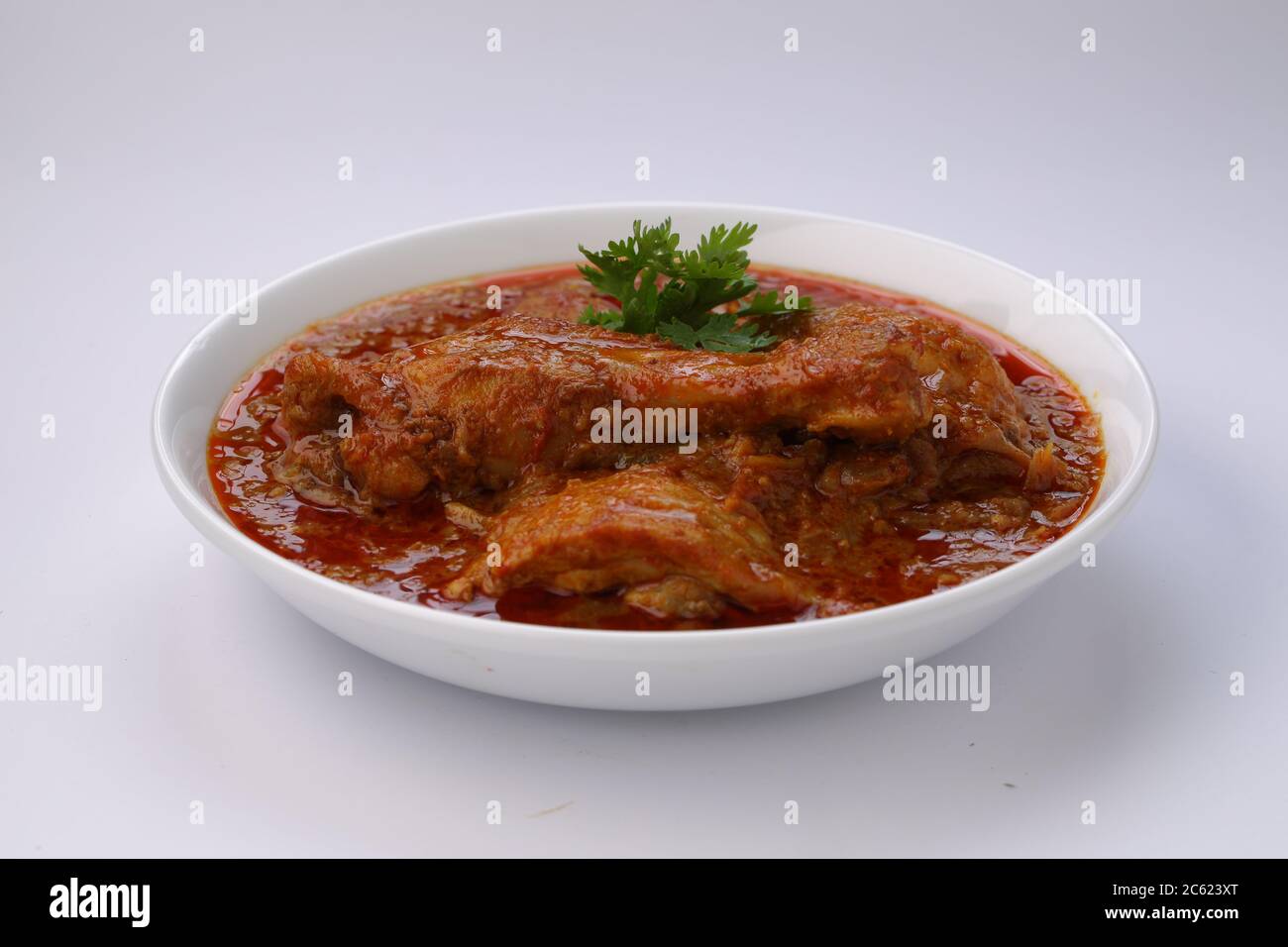 Curry de poulet ou masala, plat épicé de morceaux de poulet rouge garni de feuilles de coriandre et disposé dans un bol blanc avec fond blanc Banque D'Images