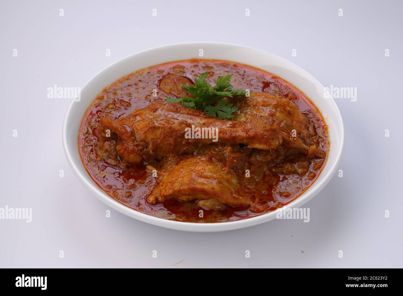 Curry de poulet ou masala, plat épicé de morceaux de poulet rouge garni de feuilles de coriandre et disposé dans un bol blanc avec fond blanc Banque D'Images