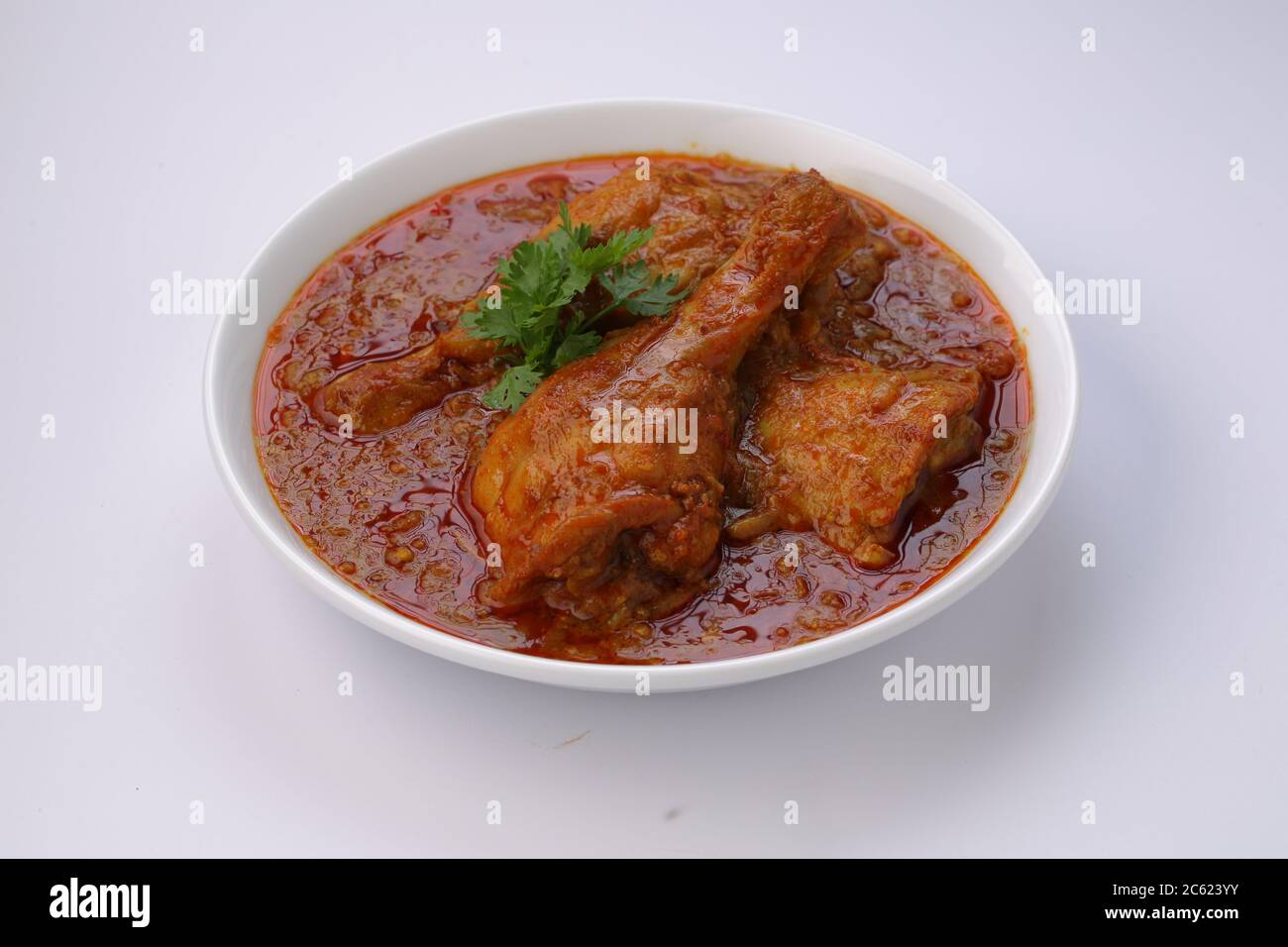 Curry de poulet ou masala, plat épicé de morceaux de poulet rouge garni de feuilles de coriandre et disposé dans un bol blanc avec fond blanc Banque D'Images