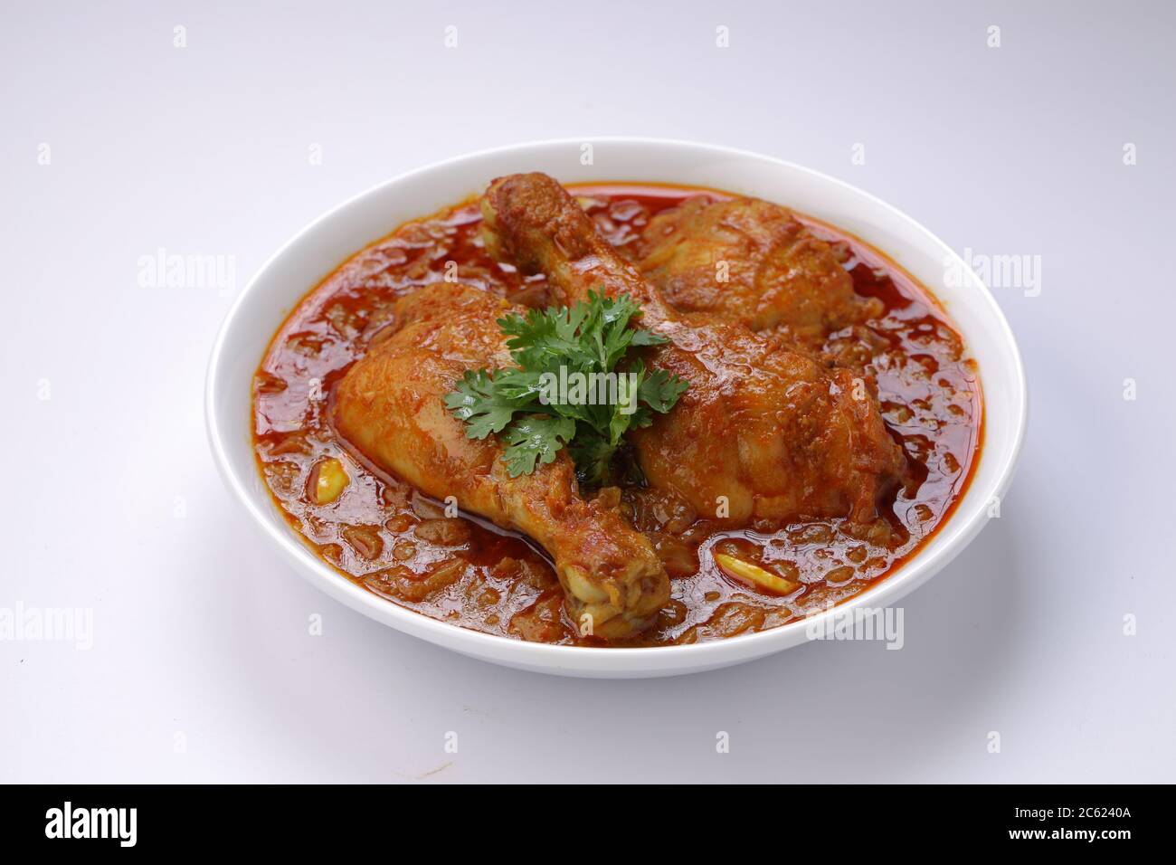 Curry de poulet ou masala, plat épicé de morceaux de poulet rouge garni de feuilles de coriandre et disposé dans un bol blanc avec fond blanc Banque D'Images
