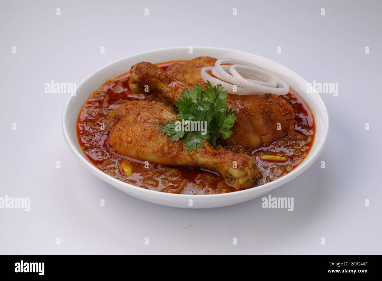 Curry de poulet ou masala, plat de poulet rouge épicé garni de feuilles de coriandre et de rondelles d'oignon disposées dans un bol en céramique blanche avec du blanc Banque D'Images