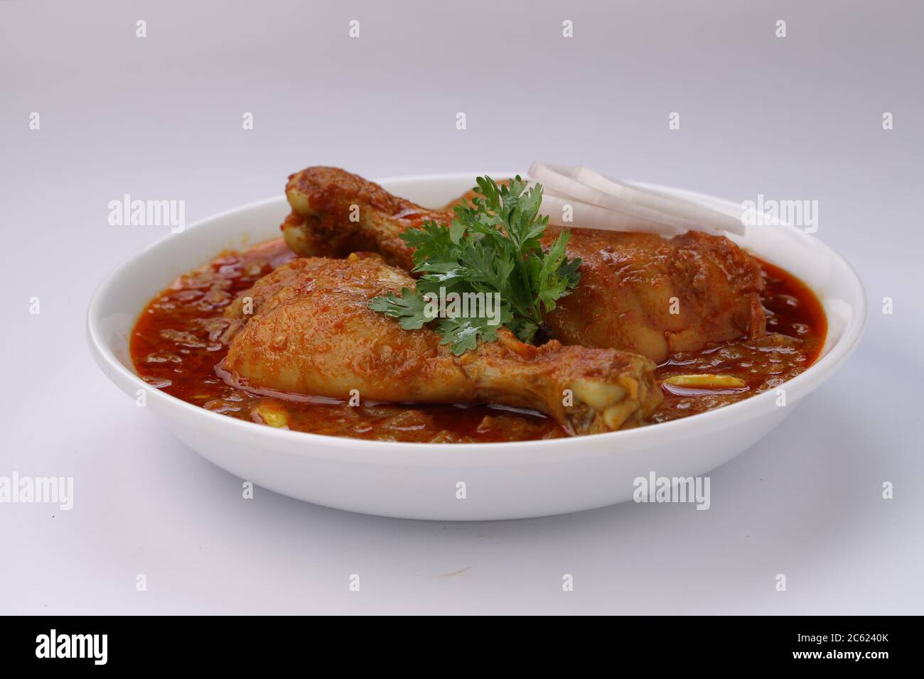 Curry de poulet ou masala, plat de poulet rouge épicé garni de feuilles de coriandre et de rondelles d'oignon disposées dans un bol en céramique blanche avec du blanc Banque D'Images