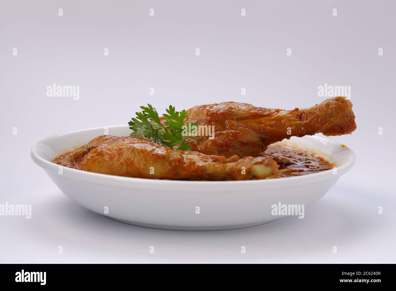 Curry de poulet ou masala, plat épicé de morceaux de poulet rouge garni de feuilles de coriandre et disposé dans un bol en céramique blanc avec du backgroun blanc Banque D'Images