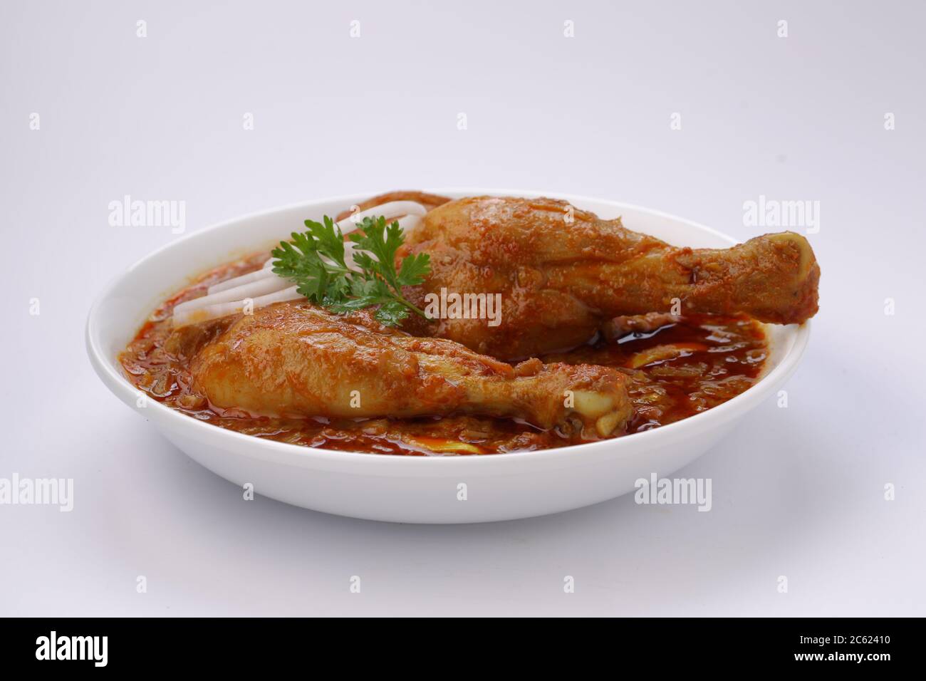 Curry de poulet ou masala, plat épicé de morceaux de poulet rouge garni de feuilles de coriandre fraîche et de rondelles d'oignon disposées dans un bol blanc Banque D'Images