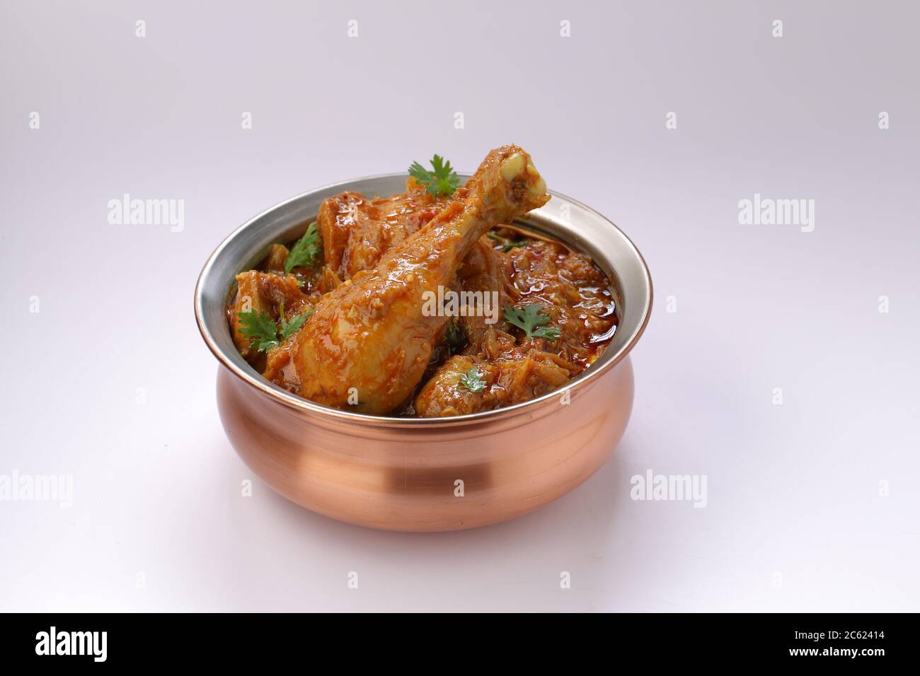 Curry de poulet ou masala, plat épicé de morceau de jambe de poulet rougeâtre garni de feuilles de coriandre, qui est traditionnellement disposé dans un bol en laiton avec wh Banque D'Images