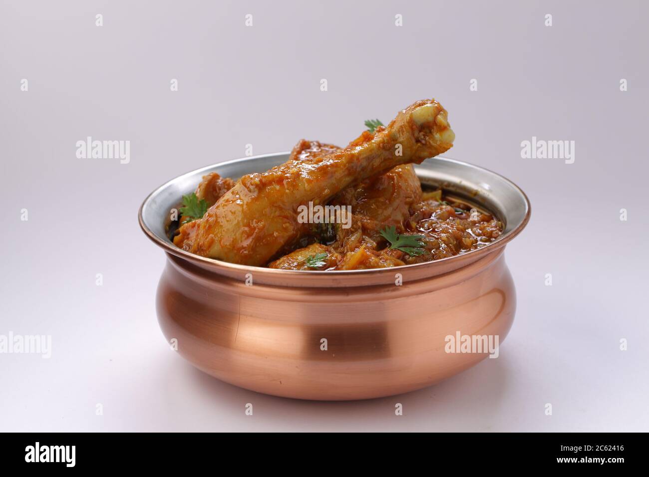 Curry de poulet ou masala, plat épicé de morceau de jambe de poulet rougeâtre garni de feuilles de coriandre, qui est traditionnellement disposé dans un bol en laiton avec wh Banque D'Images