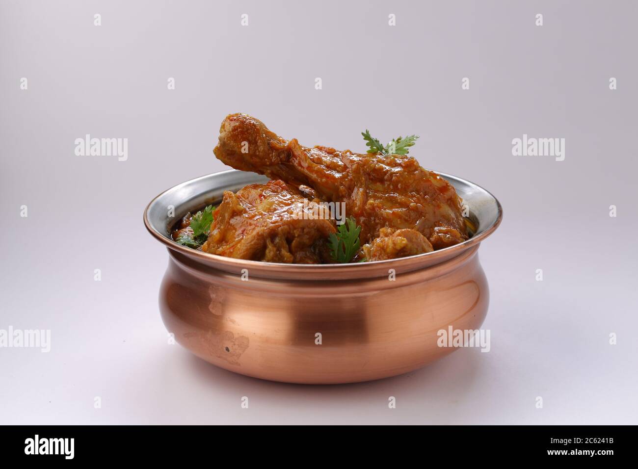 Curry de poulet ou masala, plat épicé de morceau de jambe de poulet rougeâtre garni de feuilles de coriandre, qui est traditionnellement disposé dans un bol en laiton avec wh Banque D'Images
