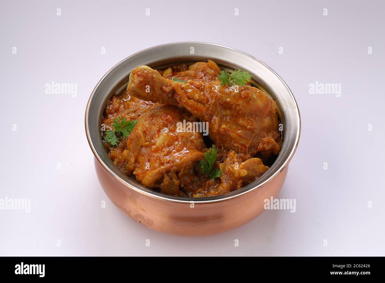 Curry de poulet ou masala, plat épicé de morceau de jambe de poulet rougeâtre garni de feuilles de coriandre, qui est traditionnellement disposé dans un bol en laiton Banque D'Images