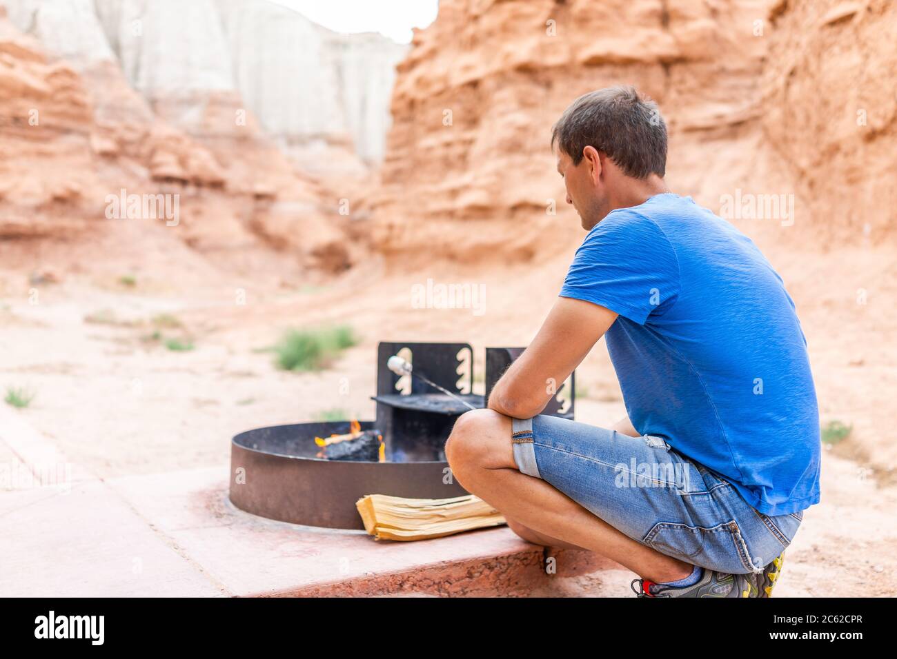 Un jeune homme torréfaction des guimauves au feu dans un barbecue de feu de camp dans le paysage désertique du parc national de Goblin Valley dans l'Utah Banque D'Images