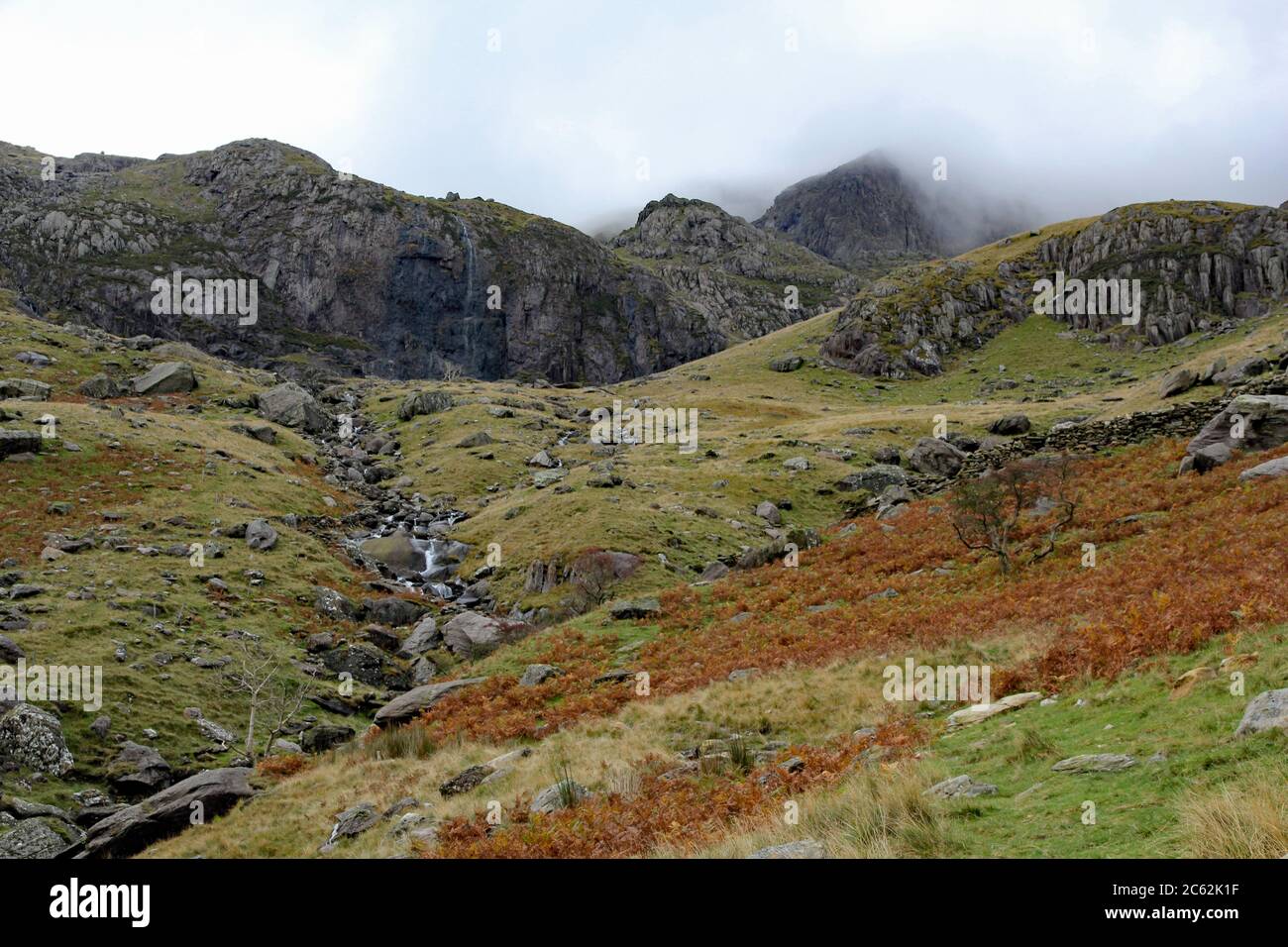 En regardant depuis Ynys Ettvers, un ruisseau de montagne mène vers Clogwyn avec Snowdon entouré de nuages, parc national de Snowdonia, au nord du pays de Galles Banque D'Images