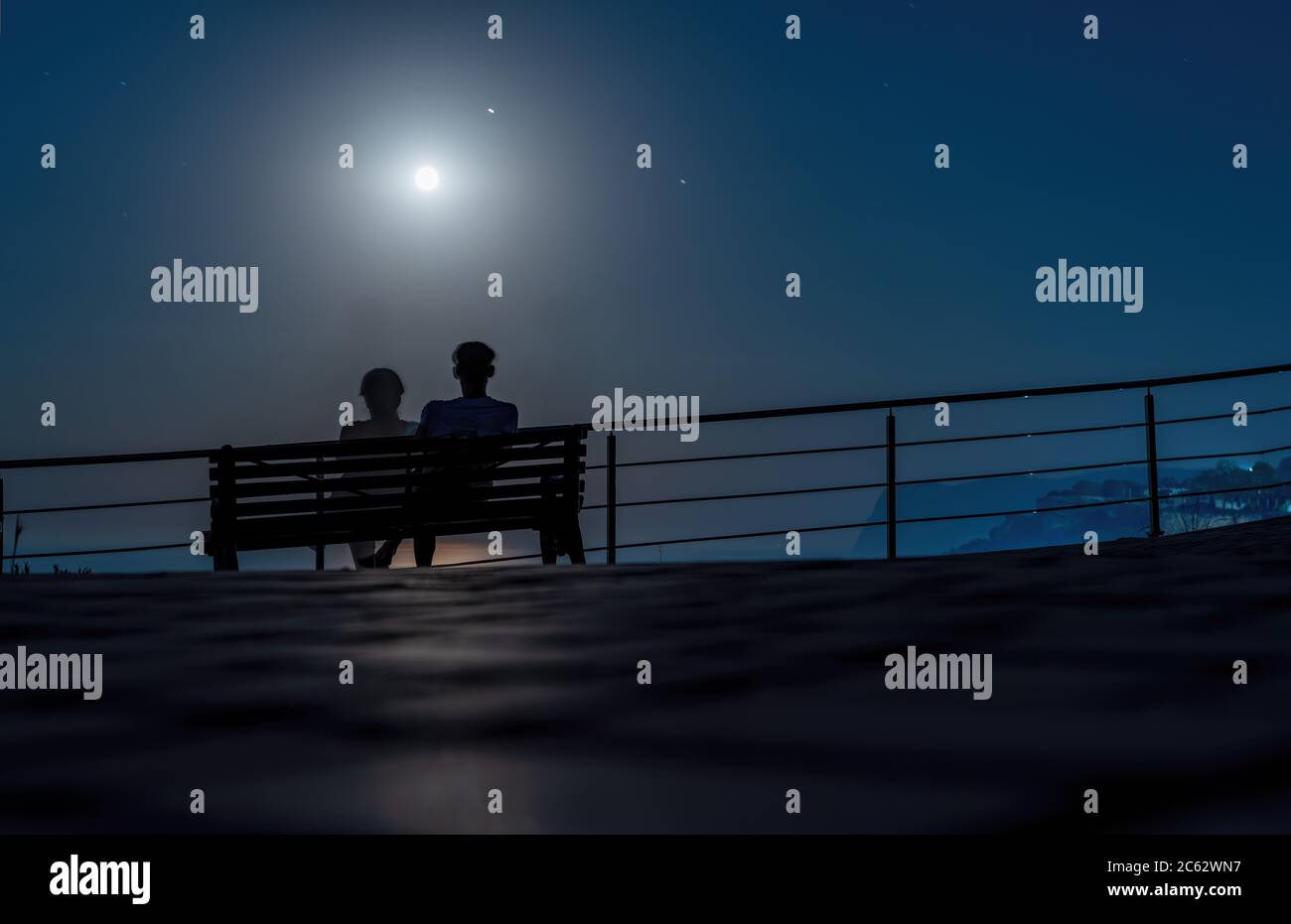 Silhouette d'un couple aimant sur un banc dans le parc sur le fond de la lune et du chemin lunaire sur la surface de l'eau. Soirée romantique sur la mer Banque D'Images