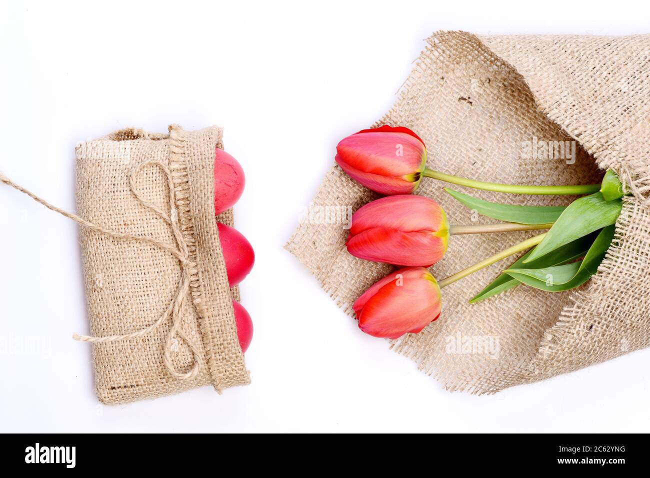 Bouquet de fleurs près des œufs de Pâques roses dans un sac rustique en toile de sacoches avec noeud. Tulipes de couleur rose ou rouge enveloppées de toile de jute sur fond blanc. Concept de vacances heureux. Bouquet de tulipes de printemps pour les vacances Banque D'Images