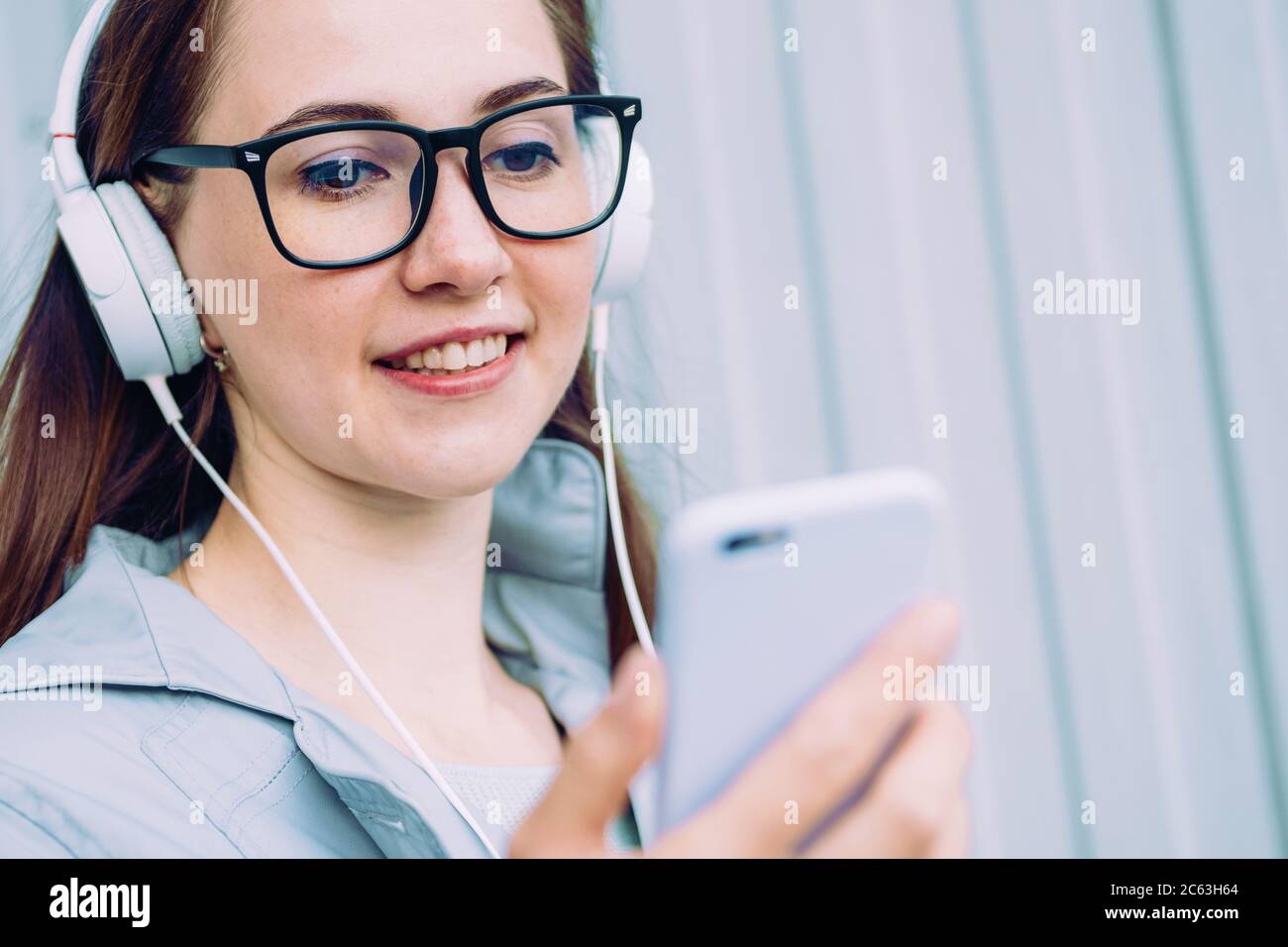 Une jeune fille de race blanche sourit et écoute de la musique tout en regardant un smartphone. Banque D'Images