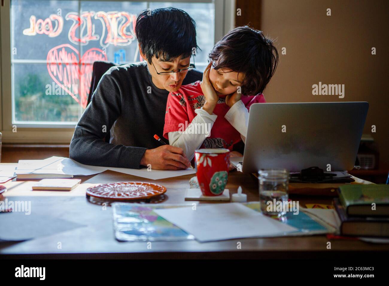 Un père travaille à la maison à la table de salle à manger avec son fils sur ses genoux Banque D'Images