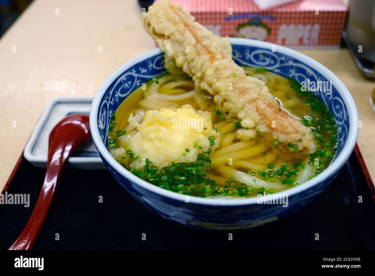 Tempura udon, avec des œufs et du chikawa dans une soupe claire, recouvert d'oignon haché placé dans un plateau noir avec une cuillère placée à côté du bol. Banque D'Images