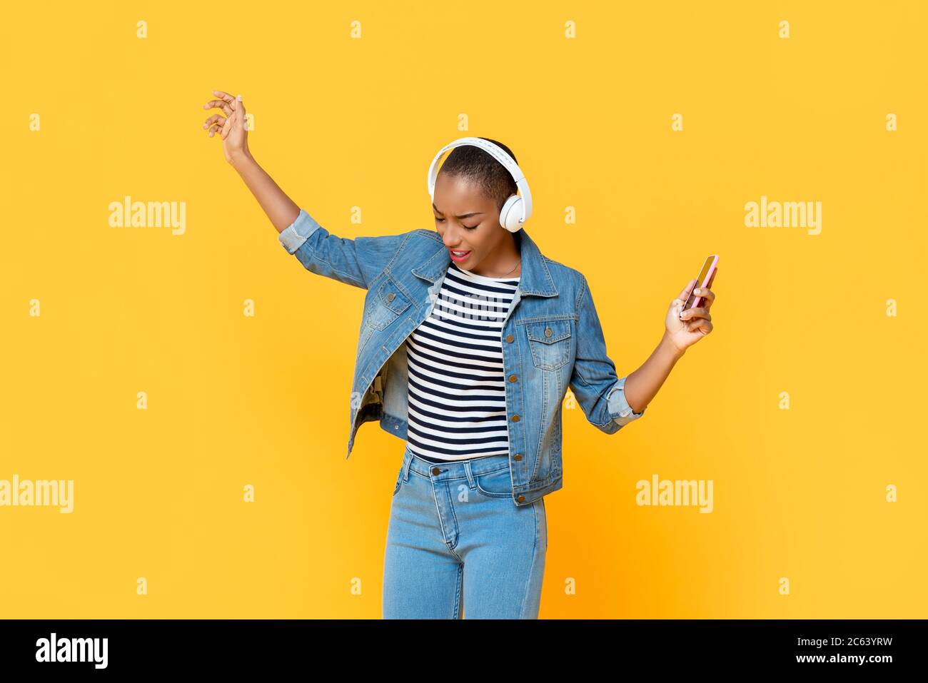 Bonne femme afro-américaine portant un casque, écoutant de la musique en ligne et dansant sur fond jaune isolé Banque D'Images