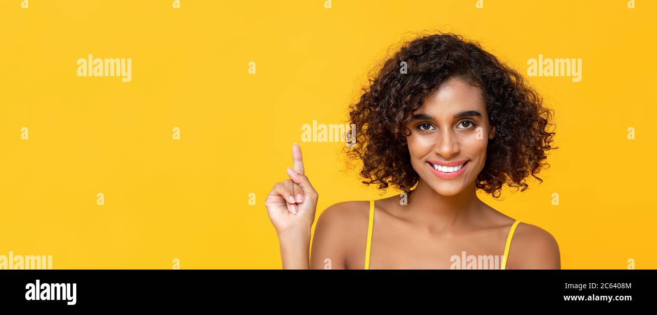 Joyeux sourire cheveux bouclés belle femme pointant de la main vers le haut pour copier l'espace isolé sur fond de bannière jaune Banque D'Images