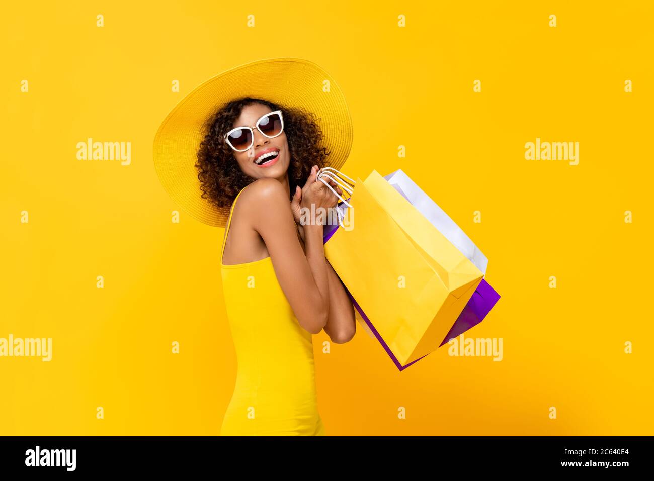 Heureuse femme surprise avec des sacs de shopping colorés souriant sur fond jaune pour l'été vente concept Banque D'Images