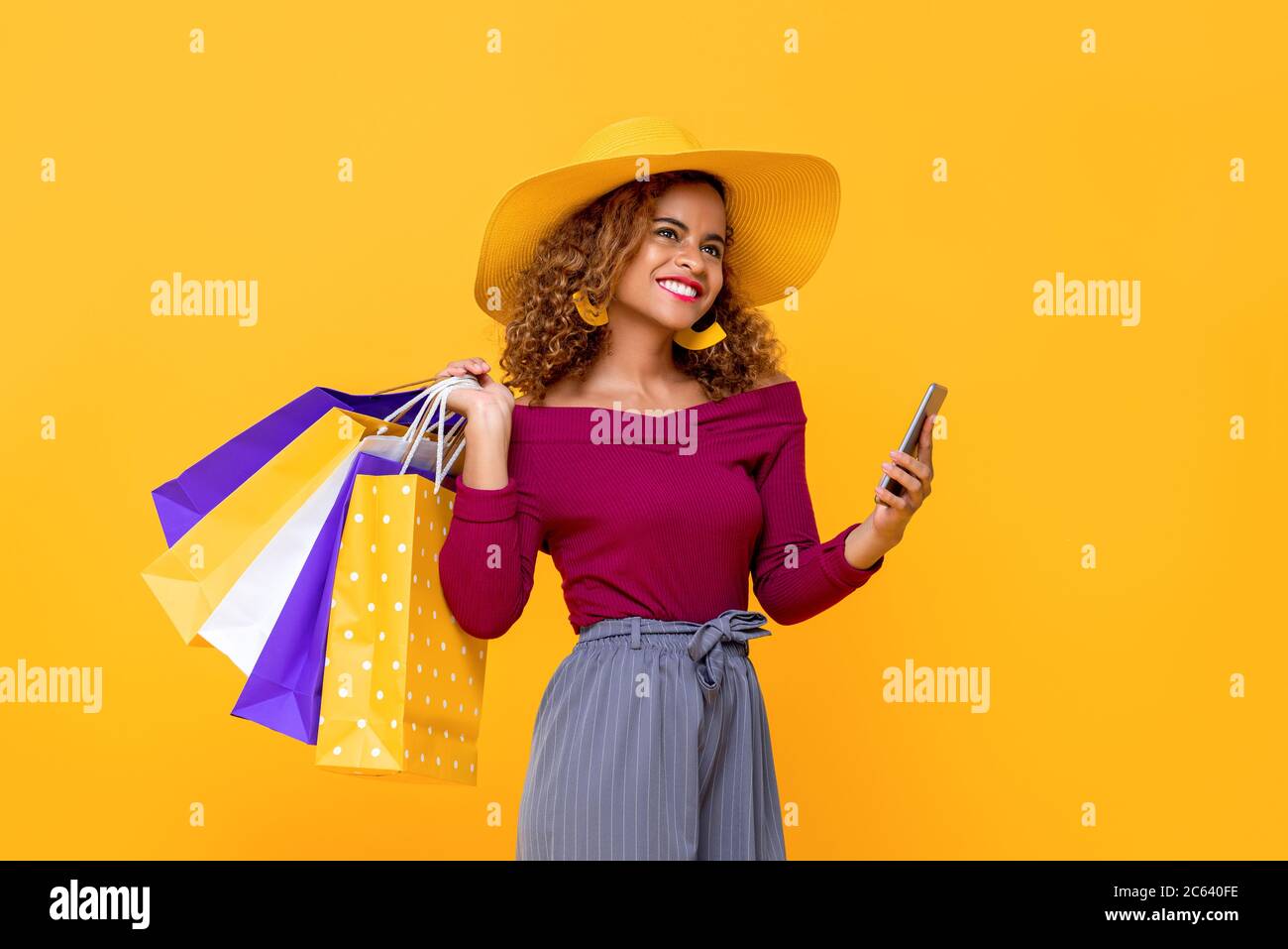 Femme de course mixte souriante à la mode avec sacs de shopping colorés et téléphone mobile isolé sur fond jaune pour l'été vente conept Banque D'Images