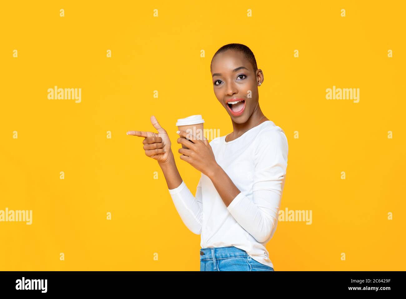 Surprise Afro-américaine femme avec un café à emporter souriant et pointant de la main vers l'espace vide à part isolé sur fond jaune Banque D'Images