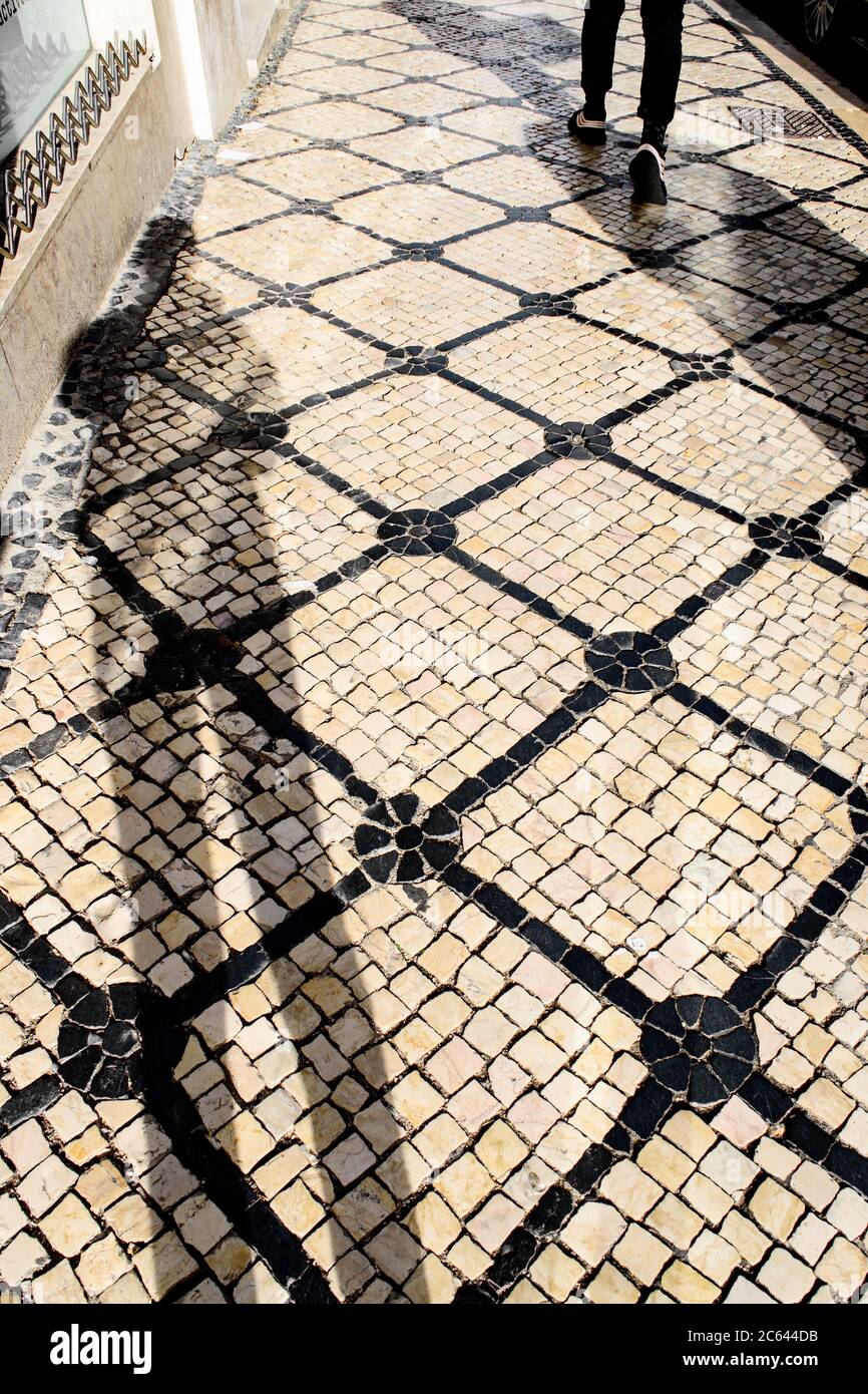 Une ombre tombe sur un trottoir de Lisbonne recouvert de pavés noirs et blancs traditionnels qui forment un motif. Banque D'Images