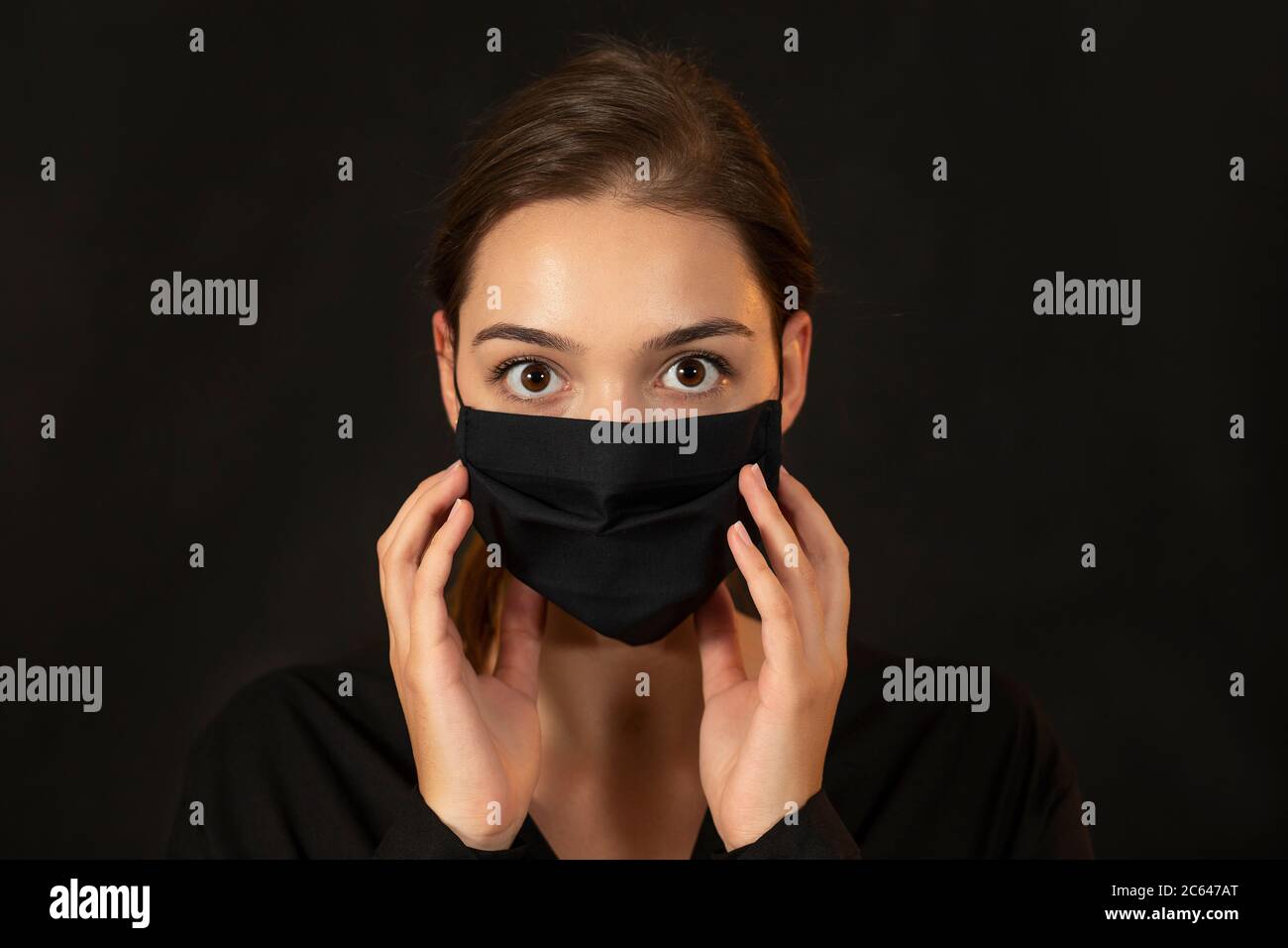Jeune femme attrayante dans un masque de protection noir sur fond sombre. Banque D'Images