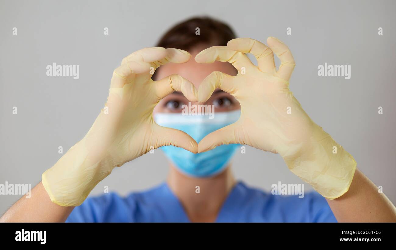 Une infirmière ou un médecin forme un cœur devant ses yeux avec ses doigts et ses mains dans des gants en latex. Banque D'Images