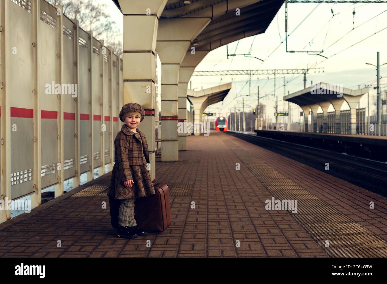 Belle charmante petite fille attendant le train à la gare tenant des bagages Banque D'Images