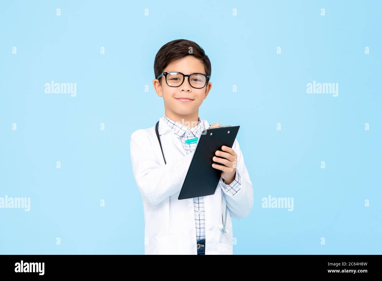 Portrait d'enfant asiatique souriant aspirant à être futur médecin écrivant la prescription dans le presse-papiers dans un fond bleu isolé Banque D'Images