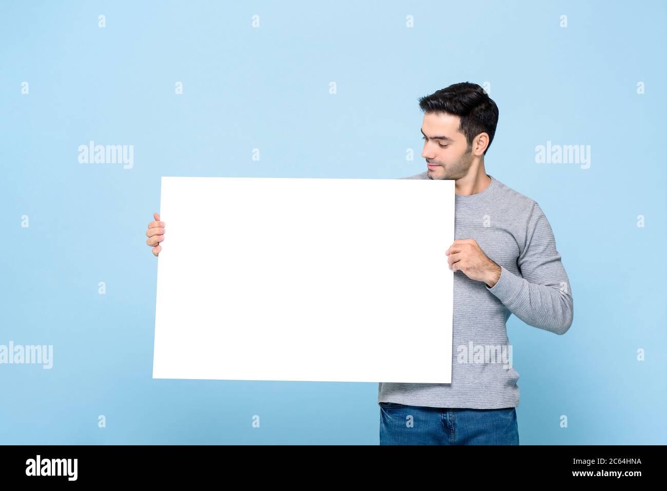 Portrait d'un beau homme caucasien tenant et regardant l'écriteau blanc sur fond bleu isolé de studio Banque D'Images